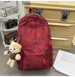 Detail des weinroten Rucksacks mit Sternmuster, KPXBD-Logo und Plüschbär-Anhänger-Dekor