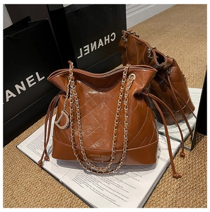 Detail of coffee brown quilted leather bucket bag with chain strap and gold D pendant