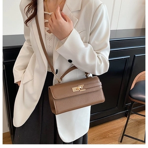 Gros plan du sac bandoulière en cuir marron avec boucle dorée porté par un mannequin