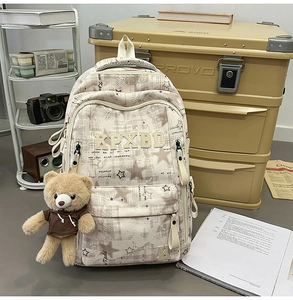 Detail eines cremefarbenen Schulrucksacks mit Sternmuster, Stickerei und Bärenanhänger