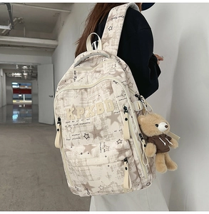 Detail eines cremefarbenen Karo-Rucksacks mit Sternmustern, Stickerei und Bärenanhänger