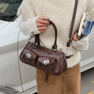 Brown faux leather Boston cylinder bag shown worn crossbody on a cream sweater