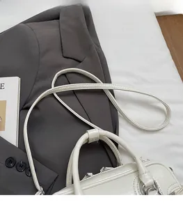 Detail of adjustable shoulder strap and leather handle on white crossbody bag