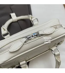 Detail of silver hardware zipper pull and smooth leather texture on white handbag
