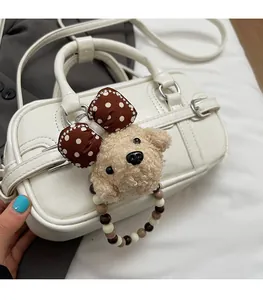Close-up of cream square handbag featuring a cute plush animal charm and beaded strap