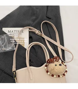 Detail of beige pebbled leather bucket bag with plush bear charm and adjustable strap