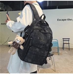 Detail eines grauen Rucksacks mit Sternmuster, 3D-Text und braunem Bären-Plüschanhänger