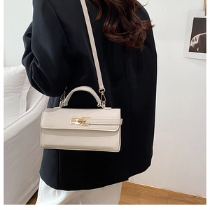 Détail du sac bandoulière beige avec fermoir doré et texture grainée sur un costume noir