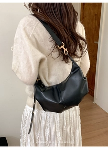 Detail of a minimalist black hobo bag with gold metal buckles and matte leather finish