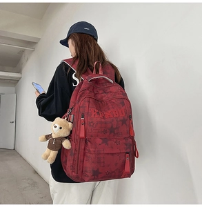 Detail eines burgunderroten Rucksacks mit Sternenmuster und süßem Bärenanhänger