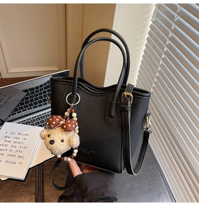 Detail of black lychee grain bucket bag featuring a wavy rim and a plush bear charm