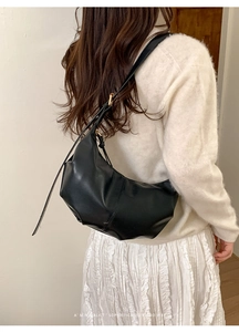 Detail of black croissant hobo bag with gold hardware accents on white knitwear