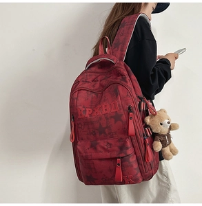 Detail eines roten Rucksacks mit Sternmuster, KPXBD-Stickerei und braunem Bärenanhänger
