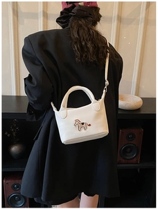 Détail du mini sac seau blanc avec broderie poney sur fond de veste de blazer noire
