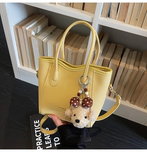 Detailed texture of yellow pebbled leather bucket bag with a plush puppy charm accessory