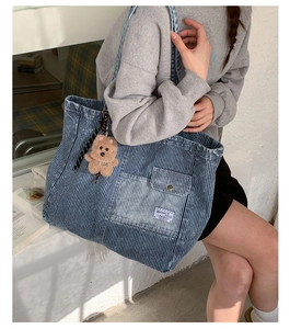 Dettaglio borsa tote in denim a righe blu con tasca esterna e ciondolo orsetto marrone