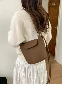 Brown leather pumpkin bucket bag shown cross-body on model with white knitwear