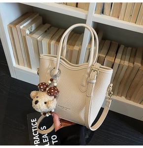 Detail of beige lychee grain bucket bag with wavy edge and cute plush bear charm