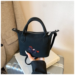 Gros plan du sac seau noir avec broderie de cheval sur des livres blancs et valise