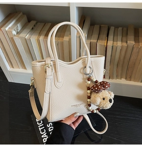 Close-up of cream leather bucket bag with litchi texture and cute dog charm accessory
