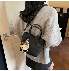 Black textured leather bucket bag with plush bear charm worn over the shoulder