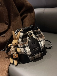 Retro geruite tweed emmertas met lederen afwerking en konijnenhanger op een leren bank
