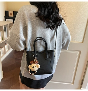 Close-up of black lychee grain leather bucket bag with cute plush bear charm detail