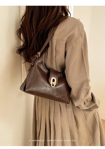 Detail shot of a dark brown retro leather tote with a gold oval metal buckle on a model