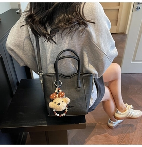 Close-up of black litchi pattern bucket bag with a cute plush bear charm accessory