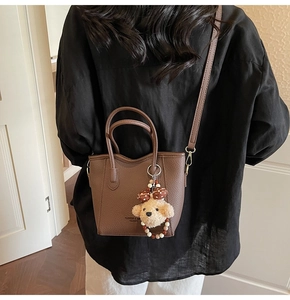 Detail of dark brown leather bucket bag with plush bear charm and fashion text engraving