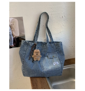 Dettaglio della borsa tote in denim a righe blu con tasca cargo e ciondolo a forma di orso