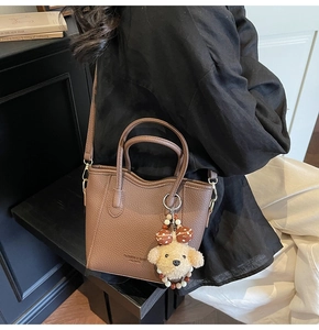 Detail of high-quality brown lychee pattern leather bucket bag with plush dog charm