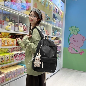 Détail du sac à dos en nylon noir avec motifs papillons et charmant pendentif d'ours en peluche