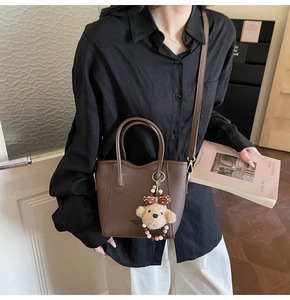 Brown bucket bag with pebble texture and cute plush bear charm in a lifestyle setting