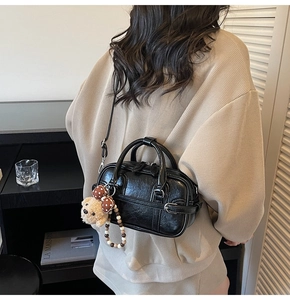 Close-up of black vintage oil-wax leather handbag with plush bear charm on a model