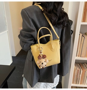 Detail of yellow lychee leather bucket bag with cute bear charm and shoulder strap