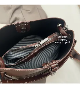 Detail of brown leather bucket bag featuring a smooth metal zipper and striped lining