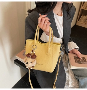 Close-up of a bright yellow bucket bag with lychee grain leather and cute teddy charm