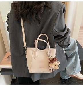 Detail of beige litchi grain bucket bag with teddy bear charm and leather strap