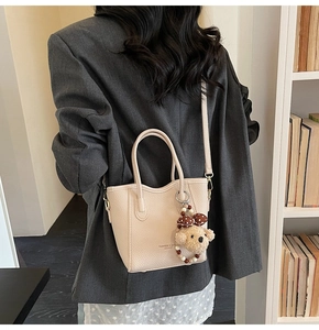 Close-up of beige lychee grain bucket bag with dog pendant and shoulder strap