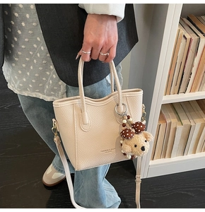 Detail of beige pebble leather bucket bag with dog plush charm and adjustable strap