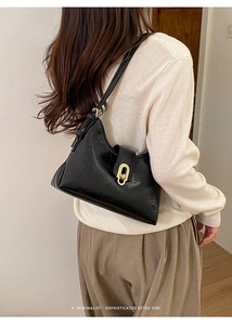 Close-up of a black glossy leather shoulder bag with a gold oval twist lock closure