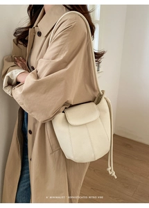 Detail of cream leather bucket bag with drawstring closure worn with a khaki trench coat
