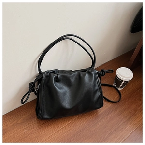 Close-up of black pleated hobo bag with knot detail and drawstring on a wooden surface