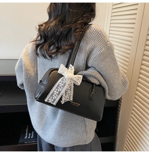 Détail du sac Boston en cuir noir avec nœud en dentelle et logo Maven & Chic porté épaule