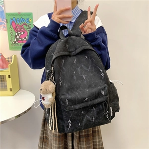 Detail of black backpack with white lightning print and a cute teddy bear plush charm