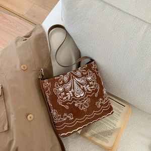 Détail du sac seau en daim marron avec broderie florale blanche et bandoulière réglable