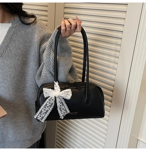 Détail du sac Boston en cuir grainé noir avec un nœud en dentelle blanche et zip doré