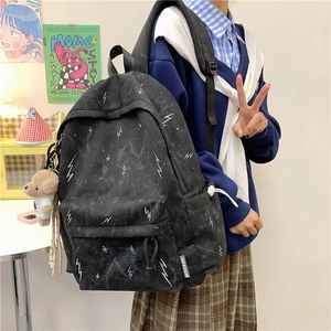 Detail of black student backpack with white lightning print and brown bear plush charm