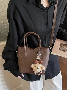 Brown litchi leather bucket bag with teddy charm and cross-body strap on model